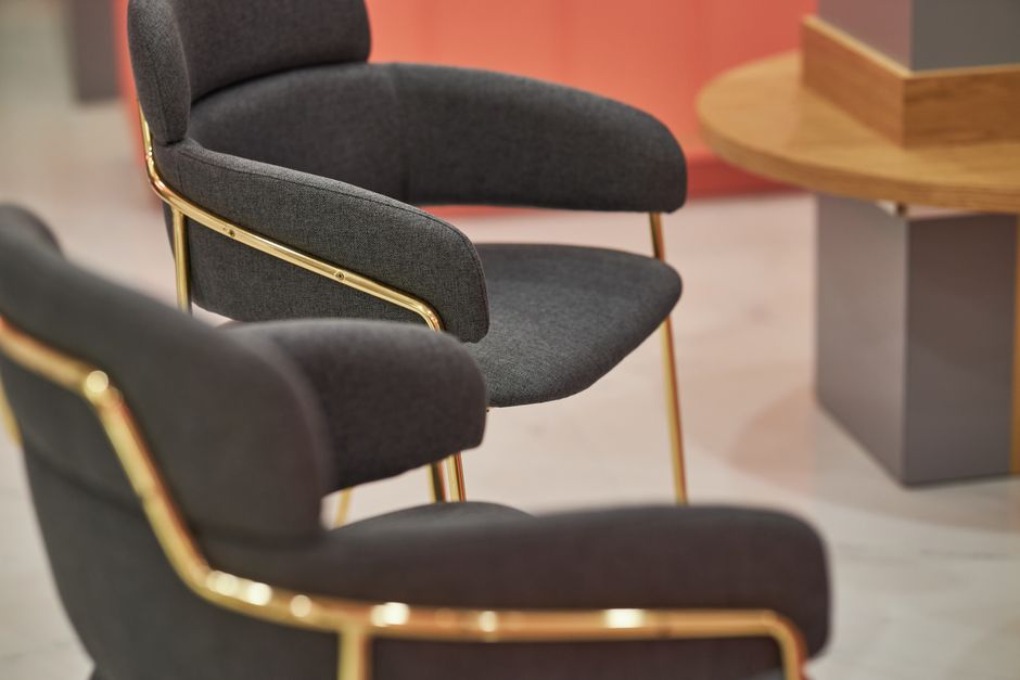 Close-up view of stylish gold-framed armchairs with gray upholstery in a contemporary office setting.